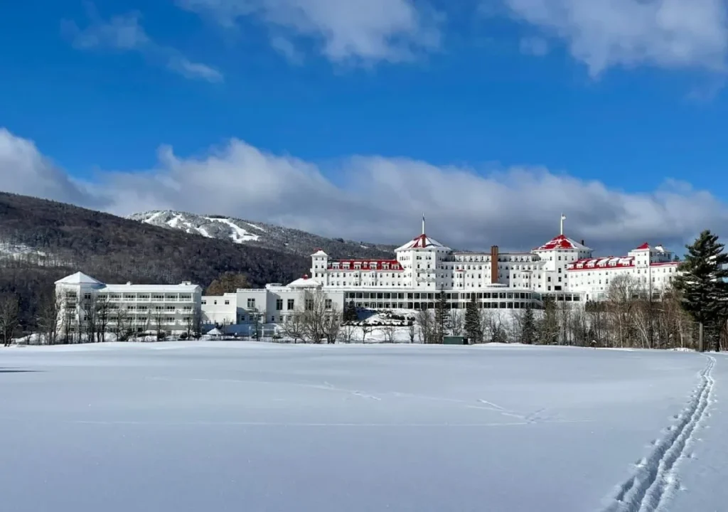 Snow-covered resort with a historic hotel and mountains in the background, ideal for winter getaways and skiing.