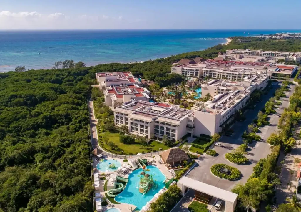 Aerial view of a luxury resort with pools, lush greenery, and ocean in the background, perfect for a tropical getaway.