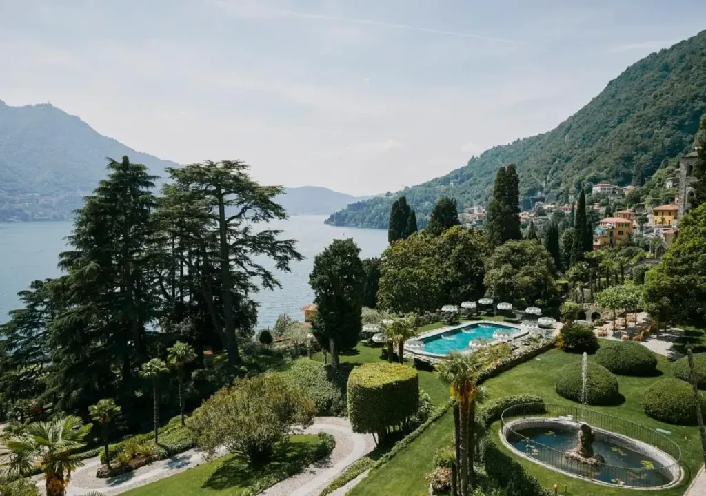 Scenic view of a lush garden by the lake, featuring a pool, fountain, and mountains in the background. Perfect for relaxation.