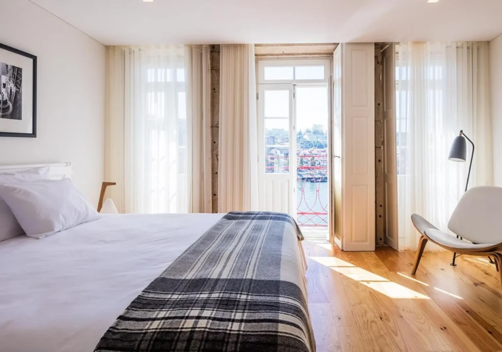 Bright and airy hotel room with a bed, natural light, and balcony views of the cityscape. Elegant and modern decor.