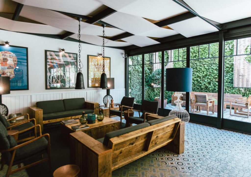 Stylish indoor lounge with modern decor, wooden furniture, and greenery visible through large windows. Cozy and inviting space.