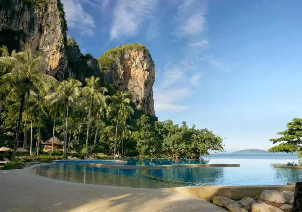 Scenic view of a tranquil lagoon surrounded by palm trees and towering cliffs under a clear blue sky. Perfect for relaxation.