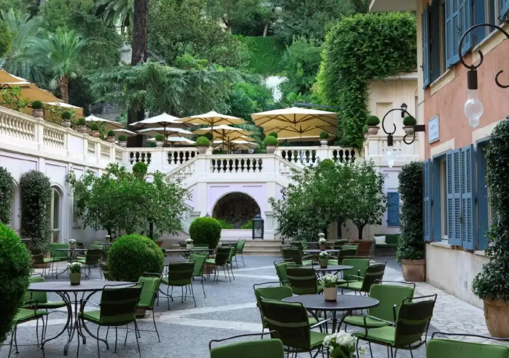 Charming outdoor café with green chairs, potted plants, and parasols in a serene garden setting. Perfect for relaxation.