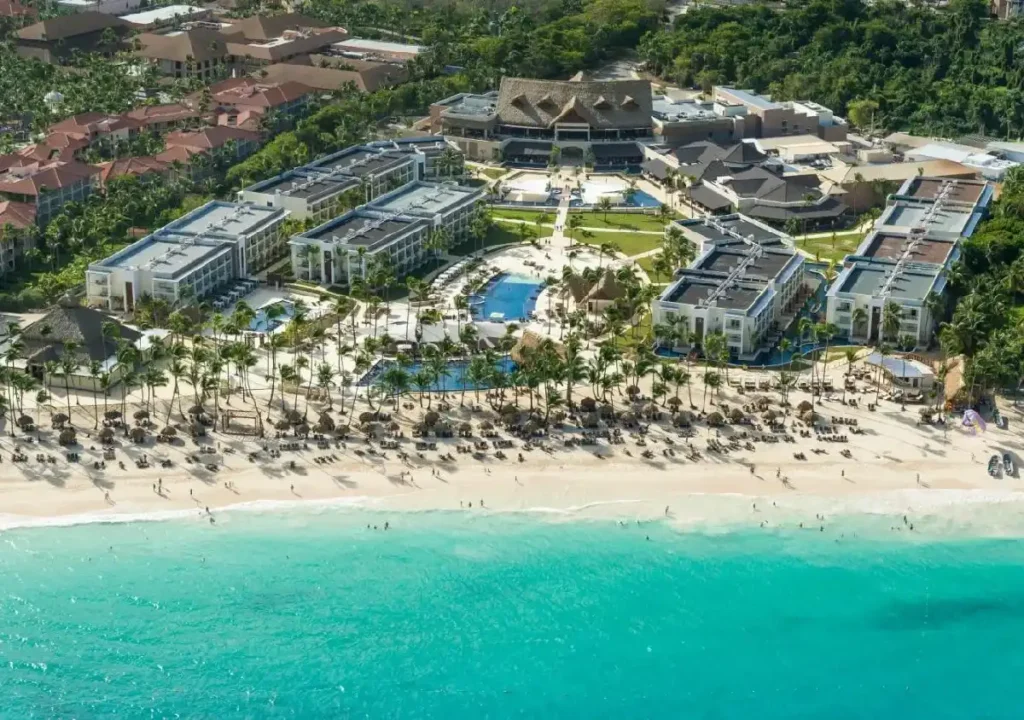 Aerial view of a luxury beachfront resort with pools, palm trees, and sandy beach, ideal for vacation relaxation.