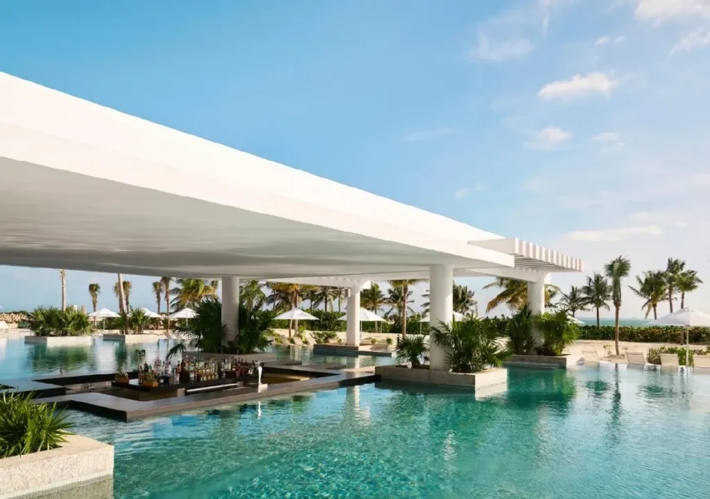 Luxurious resort pool with a stylish bar, surrounded by palm trees and blue skies, perfect for relaxation and leisure.