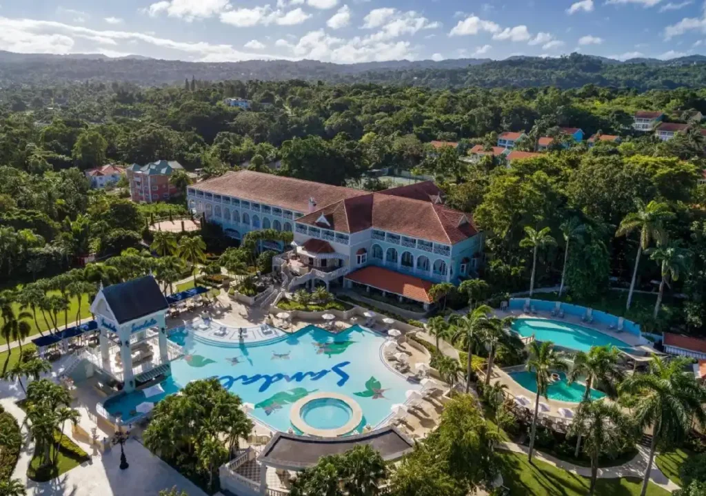 Aerial view of Sandals resort with lush greenery, tropical pools, and elegant architecture in a serene setting.