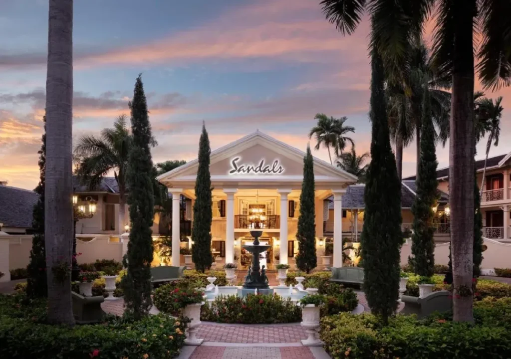Exterior view of Sandals resort at sunset, featuring gardens, fountains, and elegant architecture.