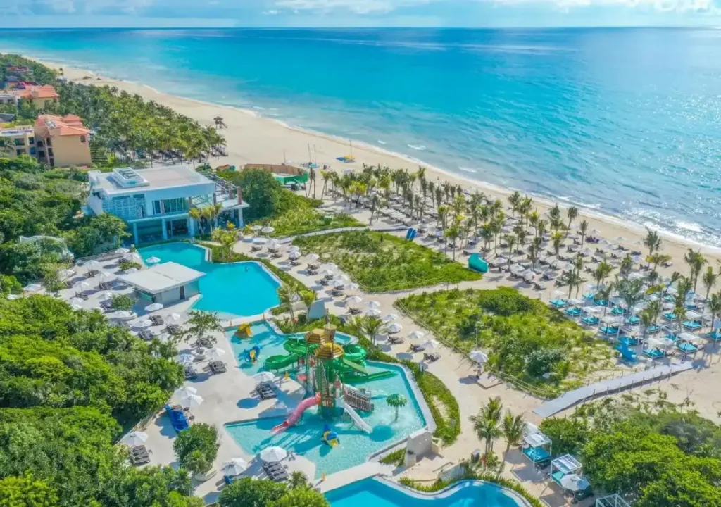 Aerial view of a beachfront resort featuring pools, a water park, and lounge areas along a pristine beach.
