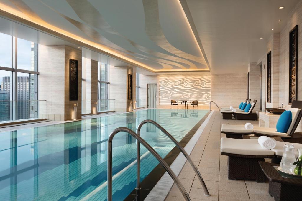 Indoor hotel swimming pool with modern design, lounge chairs, and large windows offering city views. Perfect for relaxation.