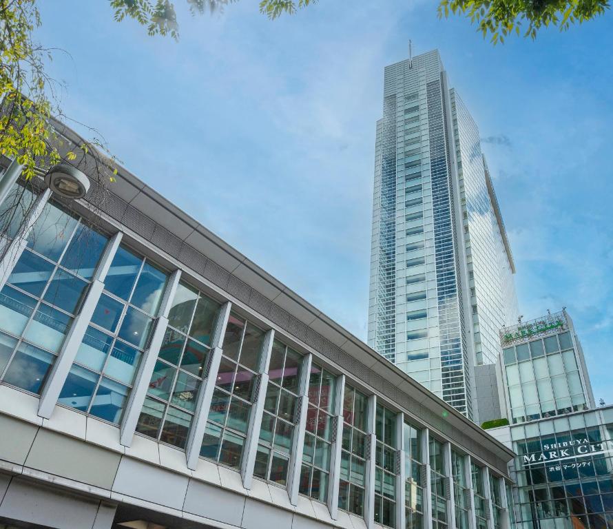 Modern glass buildings under a blue sky in Shibuya, featuring Shibuya Mark City and lush greenery.