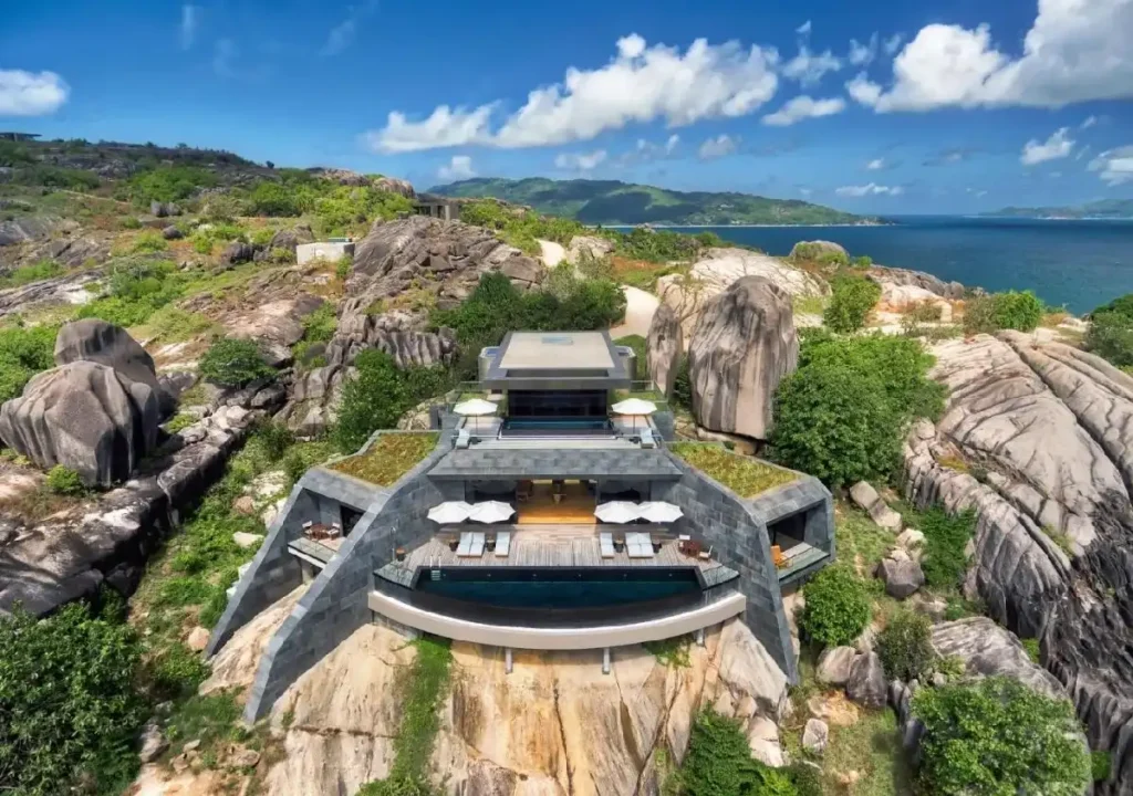 Luxury villa perched on rocky terrain, featuring modern architecture and stunning ocean views under a blue sky.