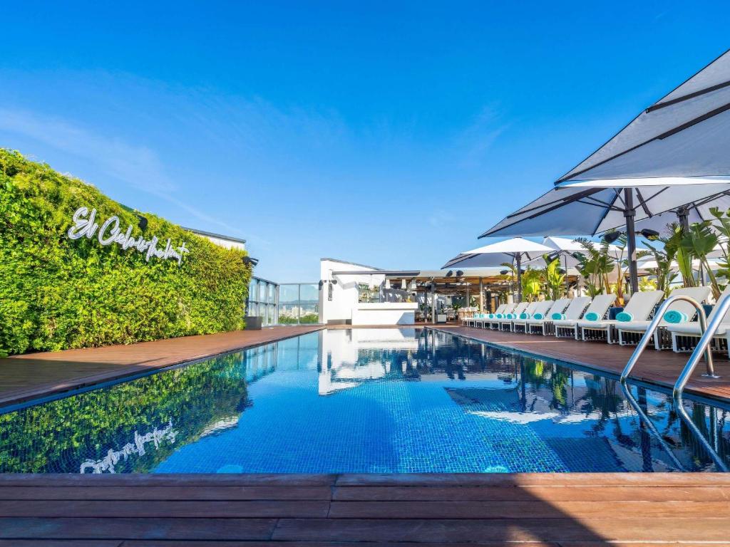Rooftop pool scene with lounge chairs, umbrellas, and lush greenery at El Cielo Hotel under a clear blue sky.