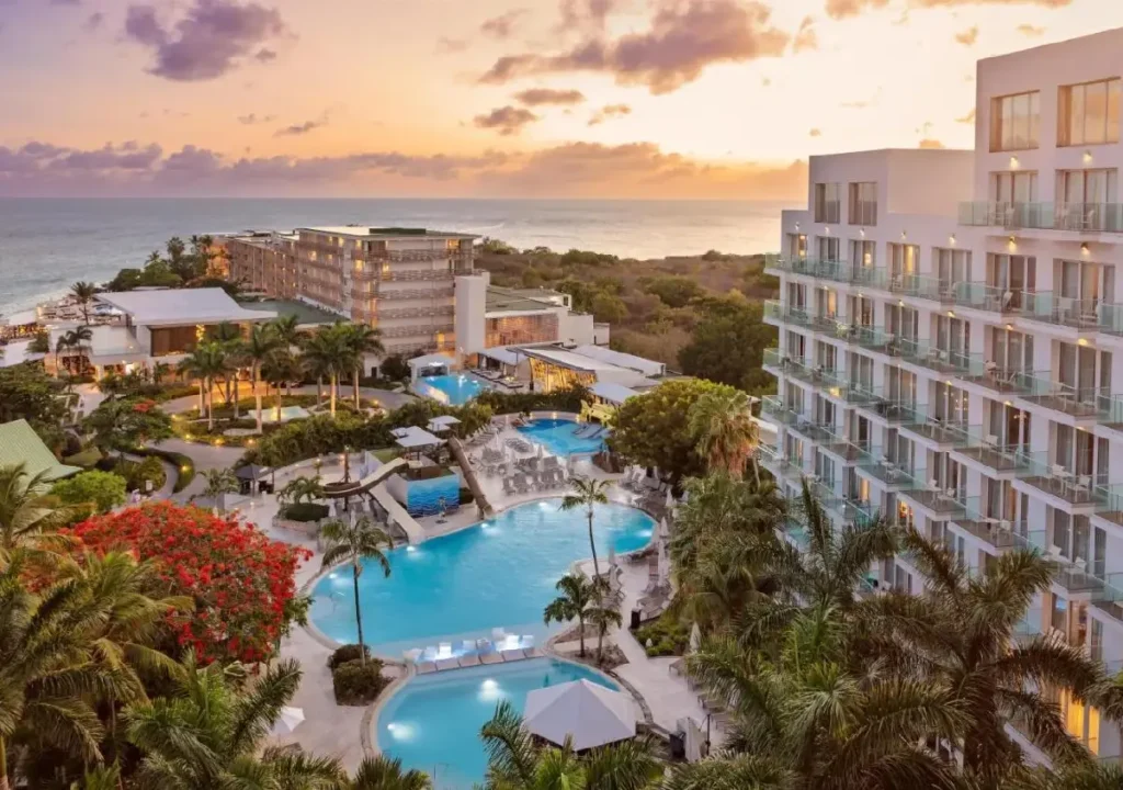 Breathtaking view of a luxury hotel at sunset, featuring sparkling pools and lush tropical landscaping by the ocean.