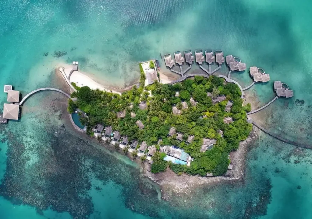 Aerial view of a tropical island resort featuring overwater bungalows surrounded by turquoise waters and lush greenery.