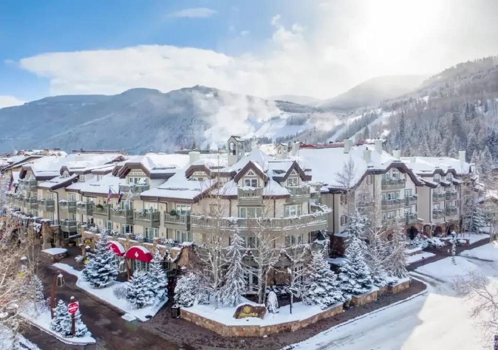 Aerial view of a snowy mountain resort with cozy architecture amidst winter landscapes and blue skies.