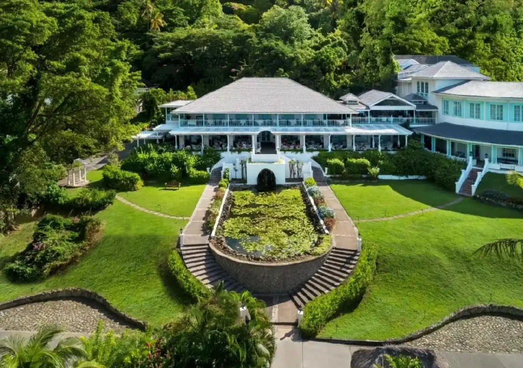 Luxurious resort with lush gardens, landscaped pathways, and a serene pond, set against a tropical backdrop.