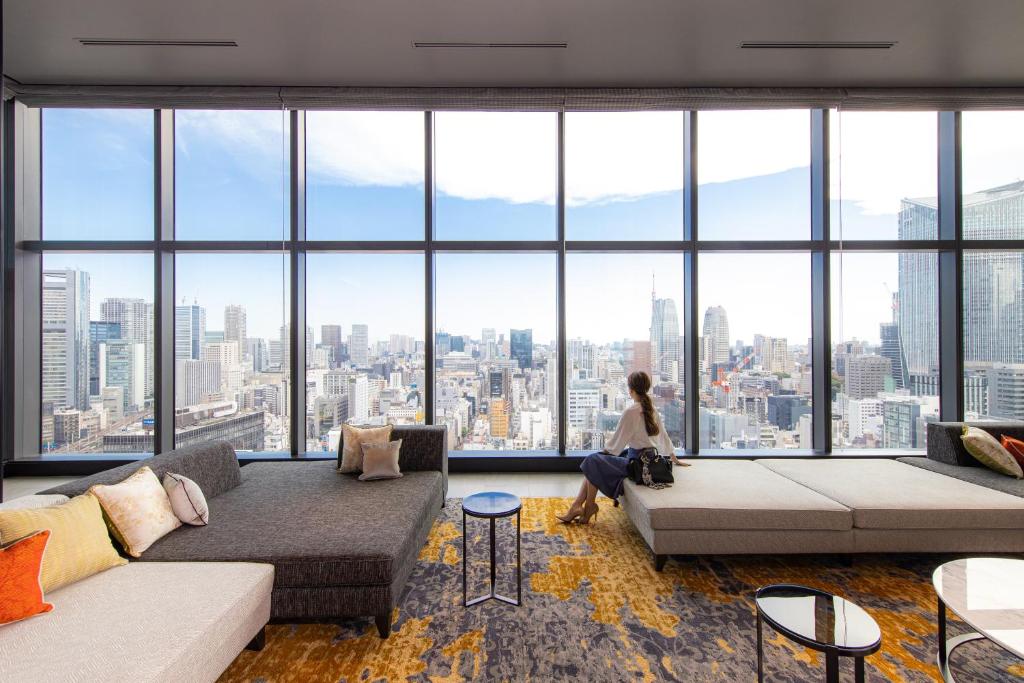 A woman gazes at a stunning city skyline from a modern high-rise lounge with elegant furnishings.