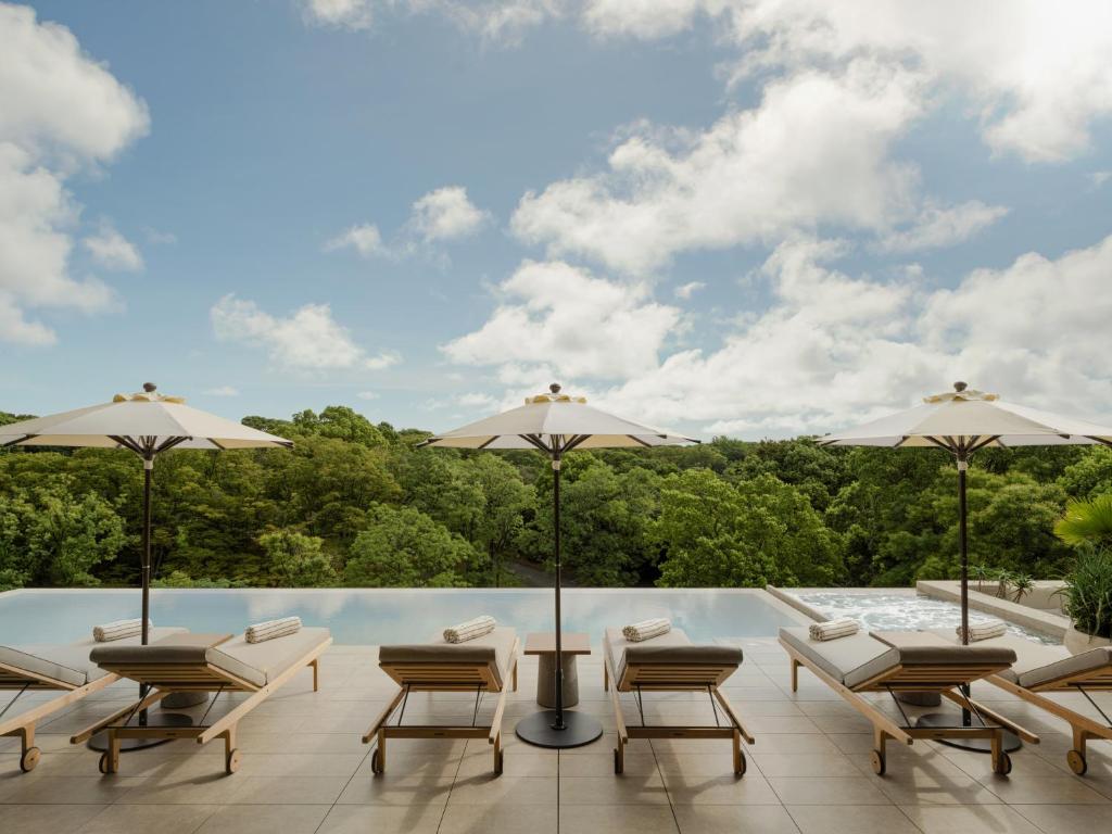 Luxurious poolside area with sun loungers and umbrellas overlooking lush greenery under a bright sky. Perfect for relaxation.