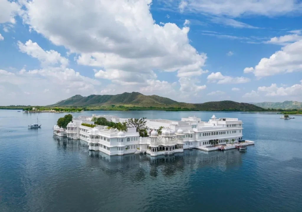 Aerial view of a stunning white palace on water, surrounded by lush hills and a clear blue sky. Ideal travel destination.