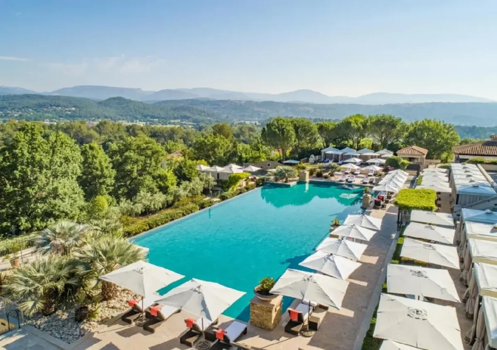 Stunning poolside view at a luxury resort, surrounded by lush greenery and mountains under a clear blue sky.