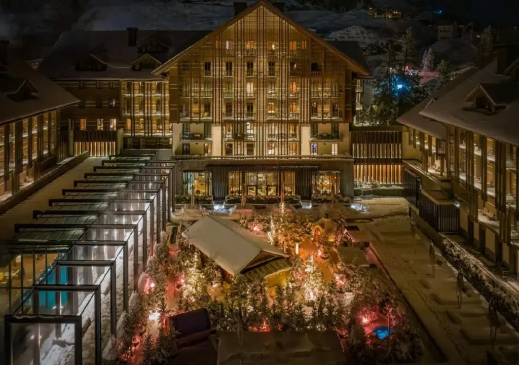 Luxurious hotel illuminated at night, surrounded by a snowy landscape and colorful garden lights, offering winter serenity.