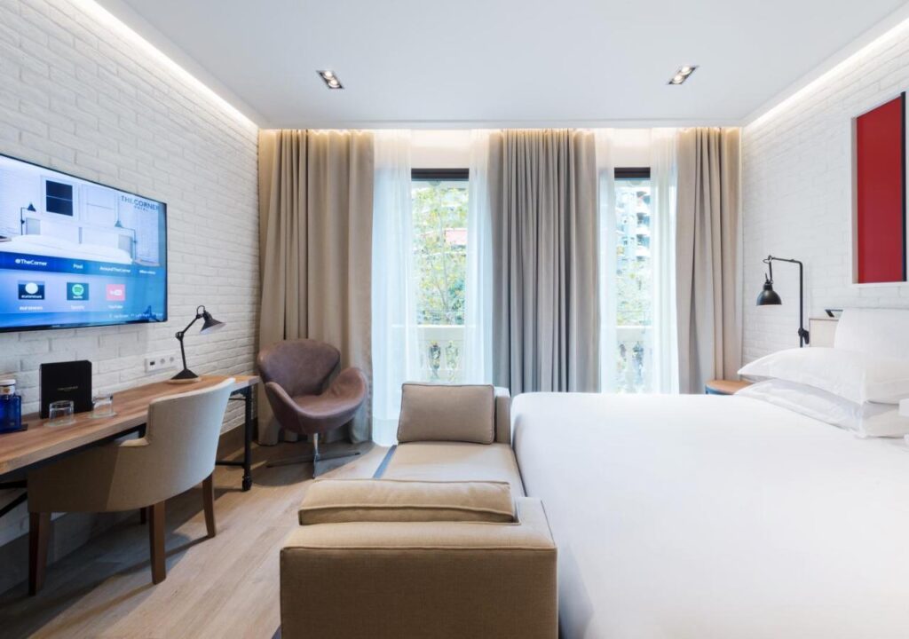 Modern hotel room featuring a cozy bed, desk, and large windows, perfect for relaxation and work.