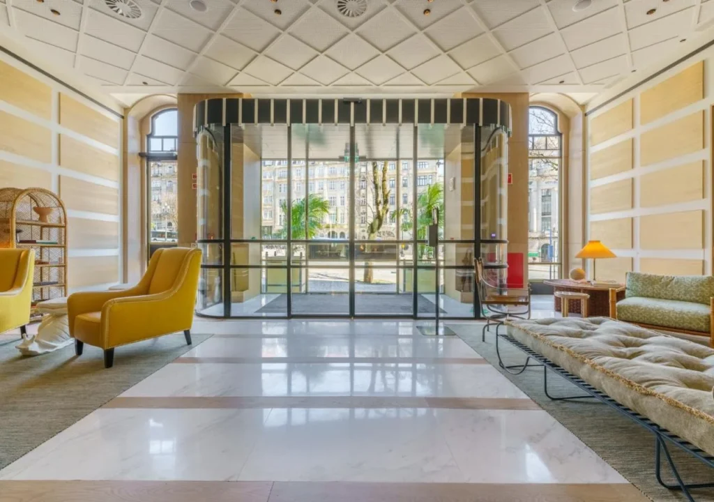 Elegant hotel lobby with yellow chairs, stylish decor, and large glass entrance, overlooking a scenic street view.