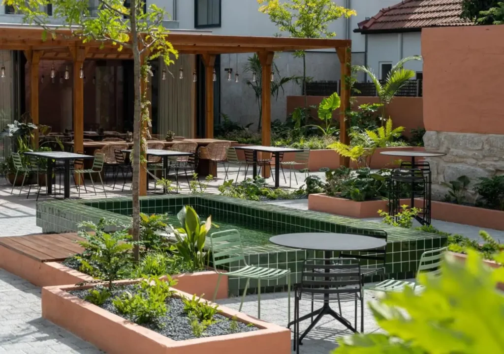 Charming outdoor cafe with lush greenery, modern seating, and a serene water feature, perfect for relaxation and dining.