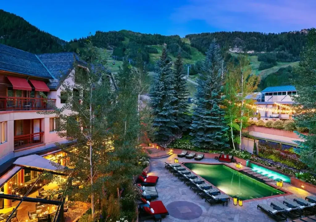 Stunning resort view with a pool, lounge chairs, and pine trees, set against a mountain backdrop at twilight.