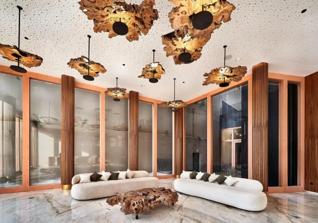 Modern lobby with unique wooden light fixtures and elegant sofas, featuring a marble floor and large glass windows.