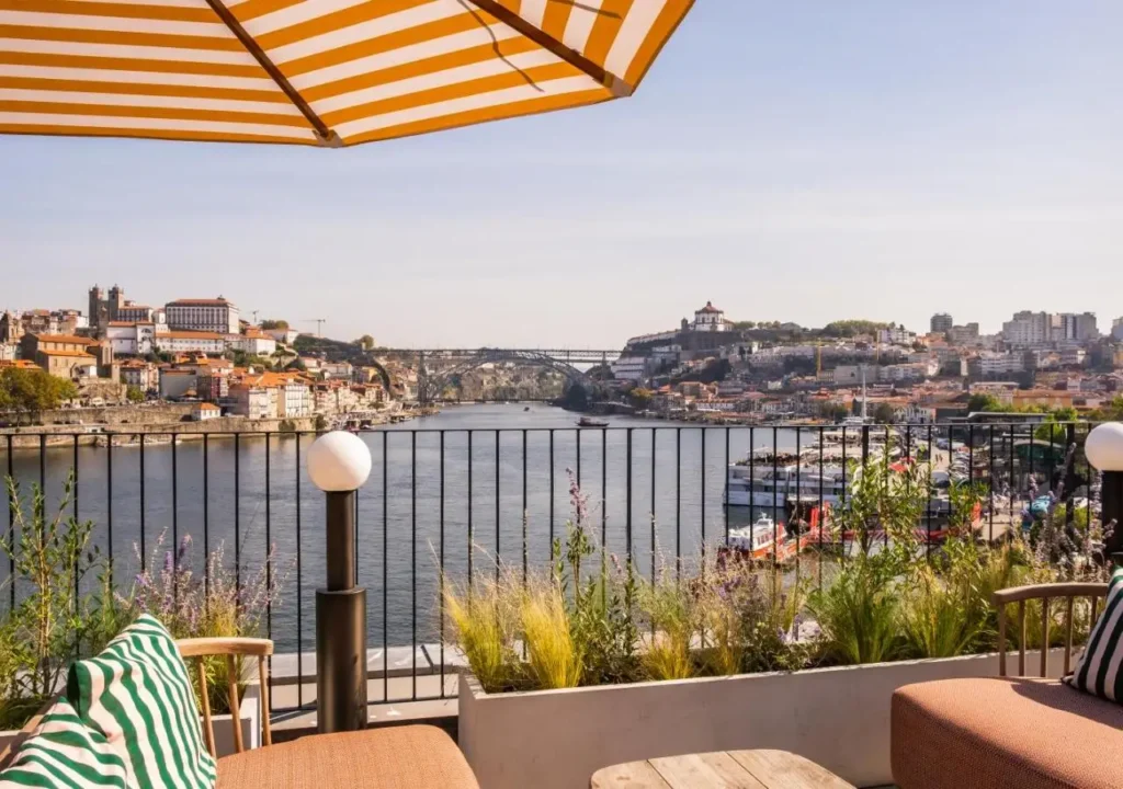 Scenic view of Porto's riverside with vibrant buildings, bridge, and terrace seating under a striped umbrella.