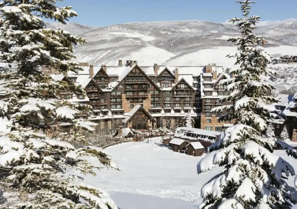Snow-covered luxury resort nestled in the mountains, surrounded by tall evergreen trees and picturesque winter scenery.