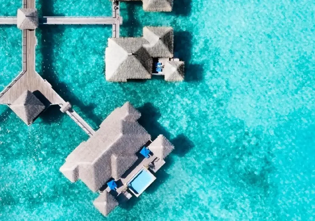 Aerial view of luxury overwater villas surrounded by turquoise waters on a sunny day, showcasing tropical paradise.