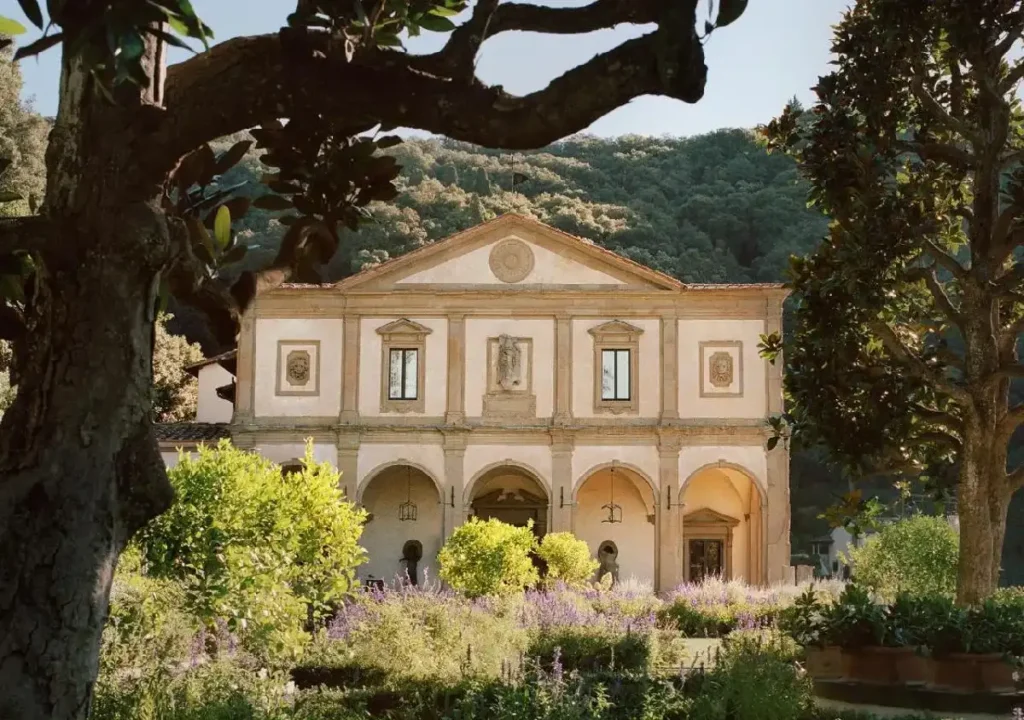 Beautiful historic building surrounded by lush gardens and mountains, showcasing elegant architecture and vibrant flora.