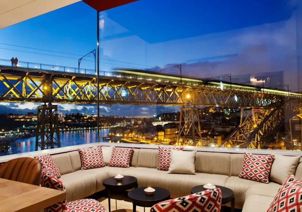 Cozy lounge area with a view of a lit bridge and river at dusk, highlighting urban beauty and stylish décor.