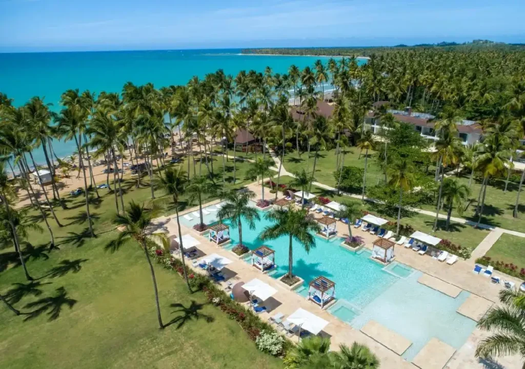 Aerial view of a tropical resort with a pool, palm trees, and a beautiful coastline in the background. Ideal for relaxation.