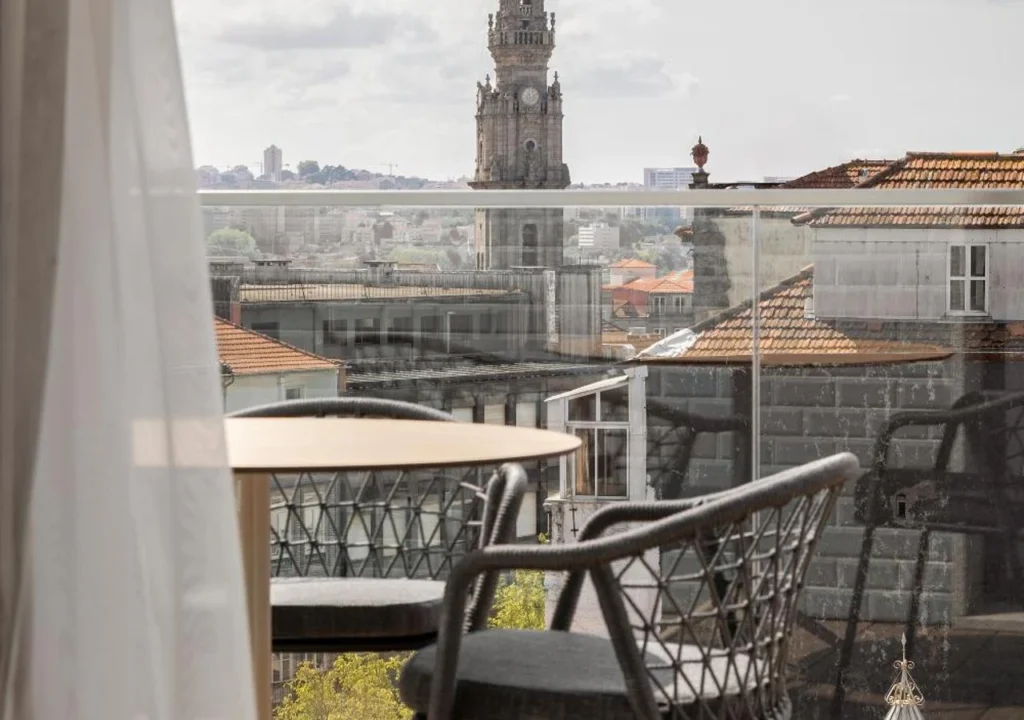 Scenic balcony view featuring a stylish table and chairs overlooking a charming city skyline with a historic tower.