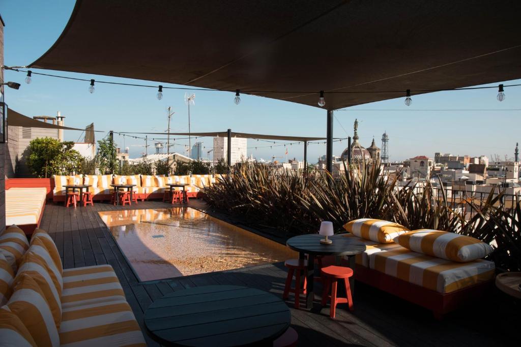Stylish rooftop lounge with striped cushions and a small pool, overlooking a city skyline and bright blue sky.