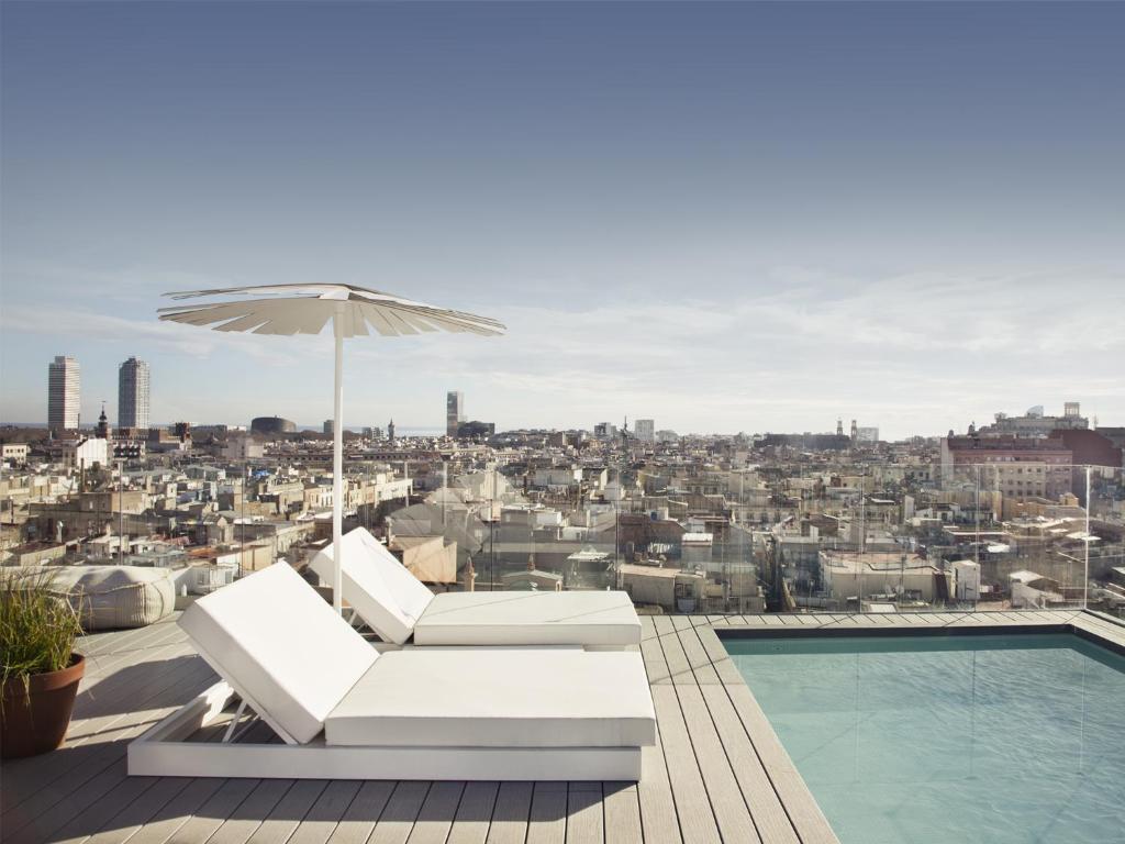 Rooftop terrace with lounge chairs and pool, offering breathtaking city views under a clear sky. Perfect for relaxation.