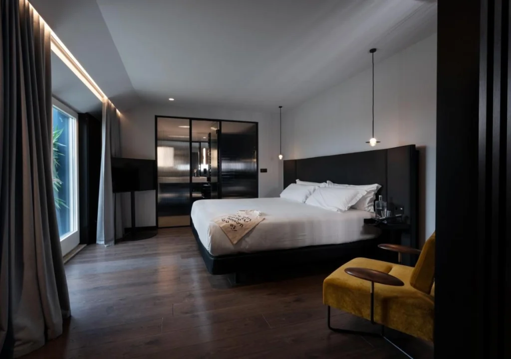 Modern hotel bedroom featuring a king-sized bed, stylish decor, and a cozy yellow chair in a serene atmosphere.