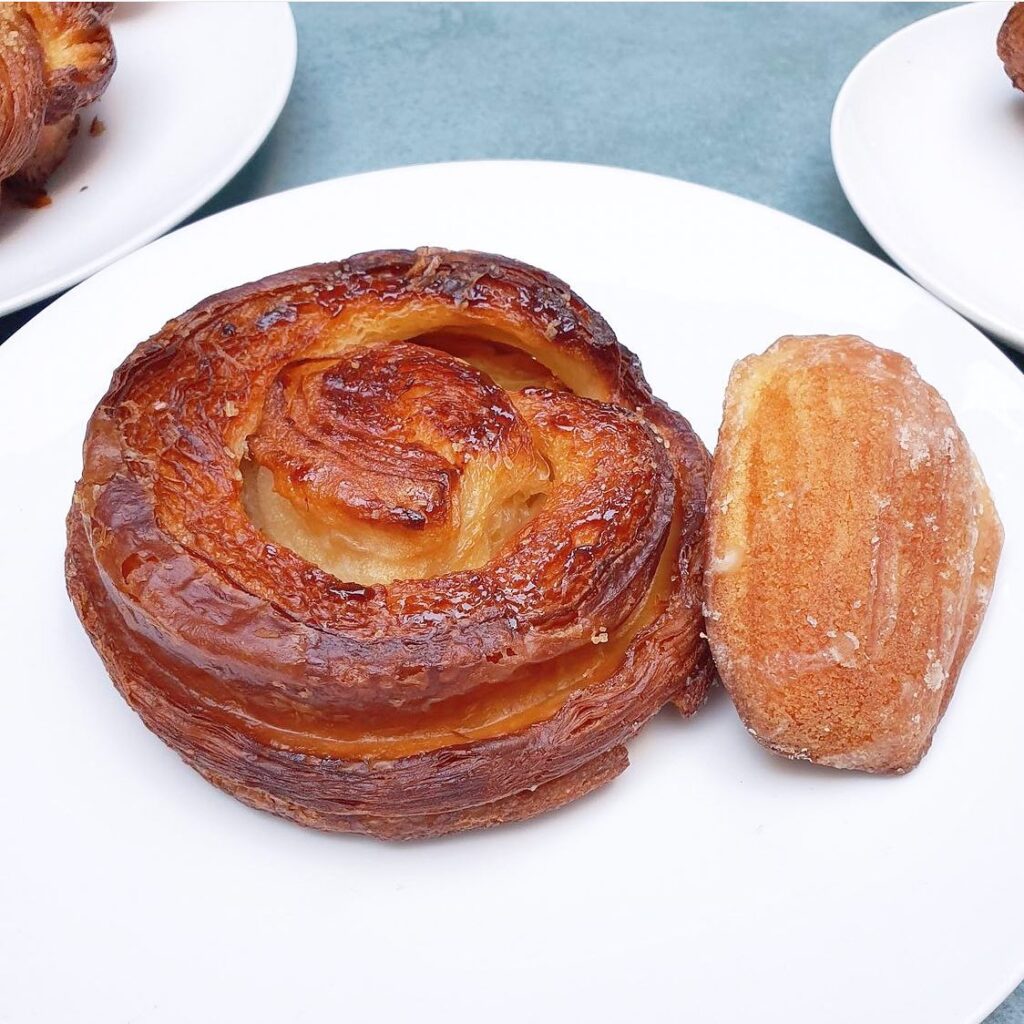 Flaky pastry and golden madeleine on white plate, showcasing delicious baked goods for dessert lovers.