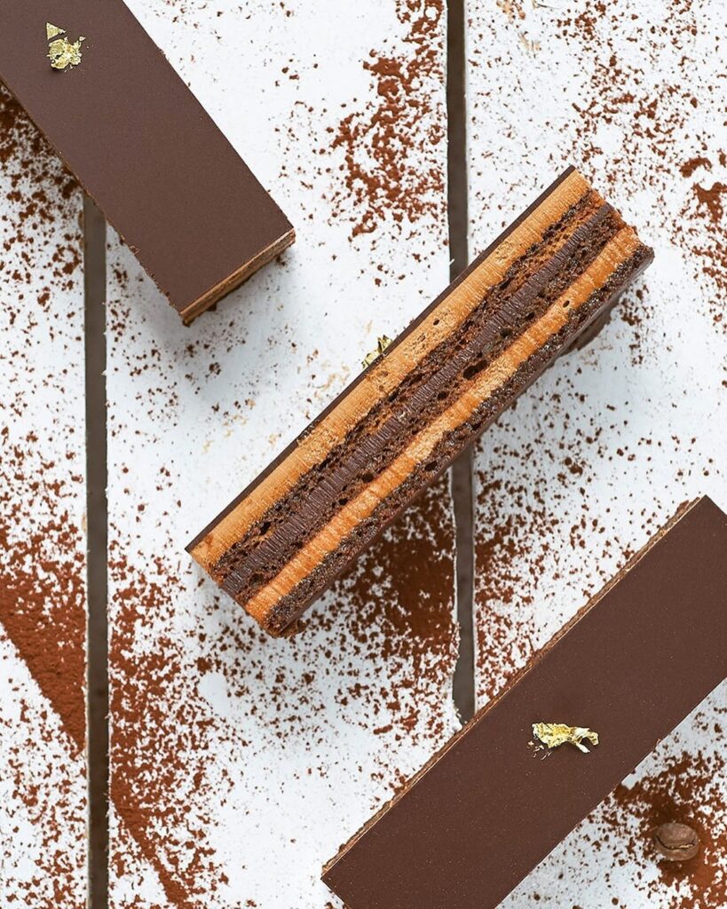 Decadent layered chocolate bars with gold leaf topping on a cocoa-dusted white surface.
