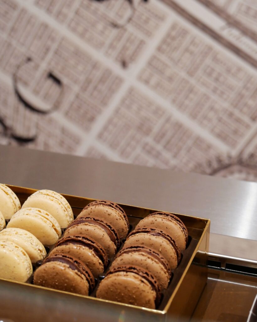 Assorted macarons in a golden box, featuring vanilla and chocolate flavors on display at a patisserie.
