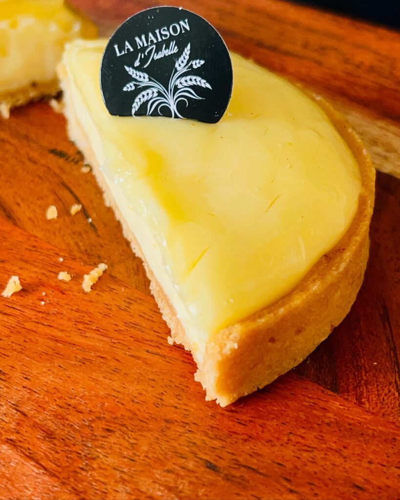 Slice of creamy custard tart with a La Maison d’Isabelle label on a wooden board.