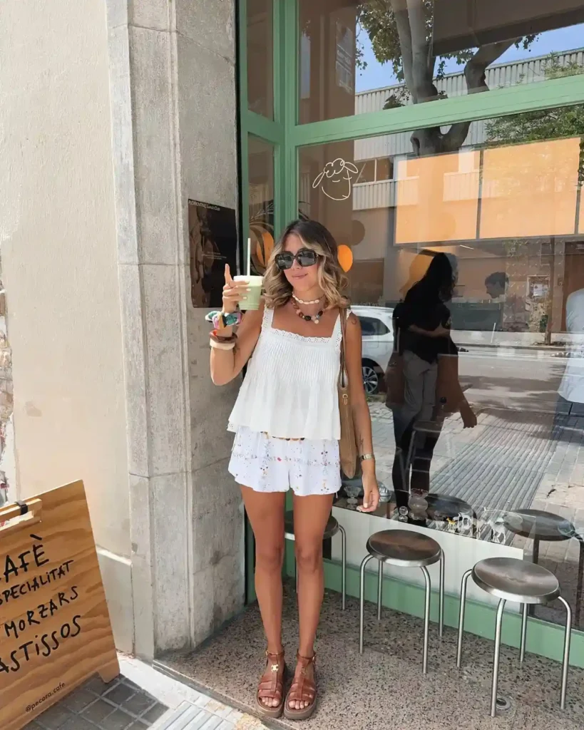 Young woman in stylish summer outfit holding a drink outside a café, featuring a casual, vibrant urban setting.