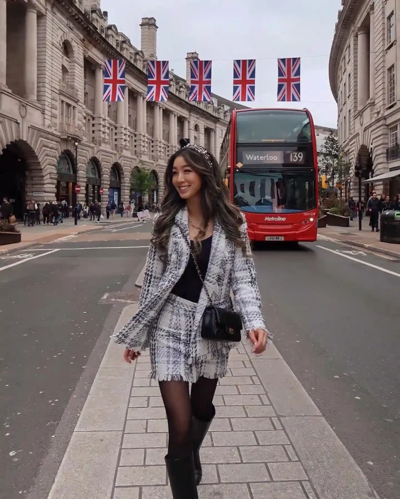 A stylish woman walking in London, wearing a chic outfit, with a red double-decker bus and British flags in the background.