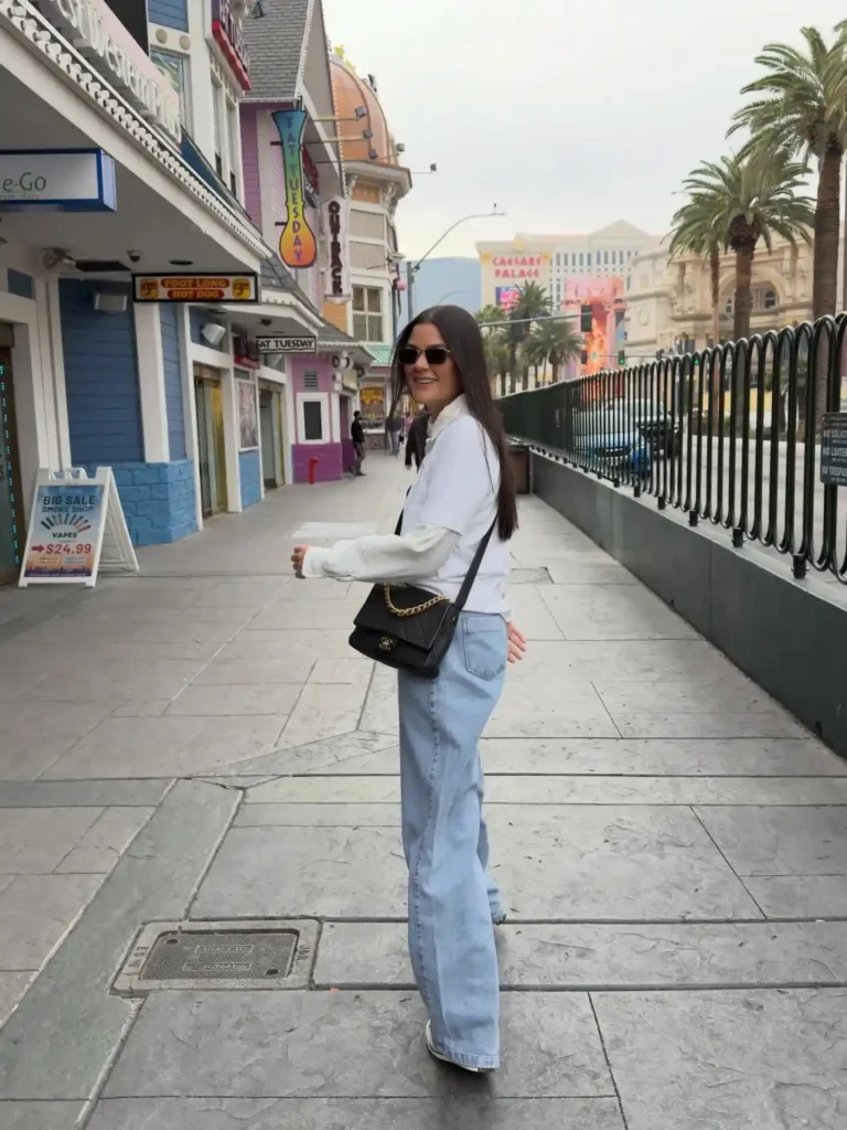 Young woman smiling on a lively street in Las Vegas, wearing casual style with palm trees in the background.