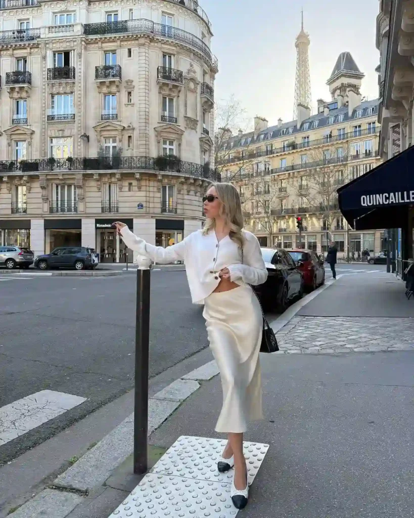 Stylish woman poses on a Paris street, featuring elegant buildings and the Eiffel Tower in the background.