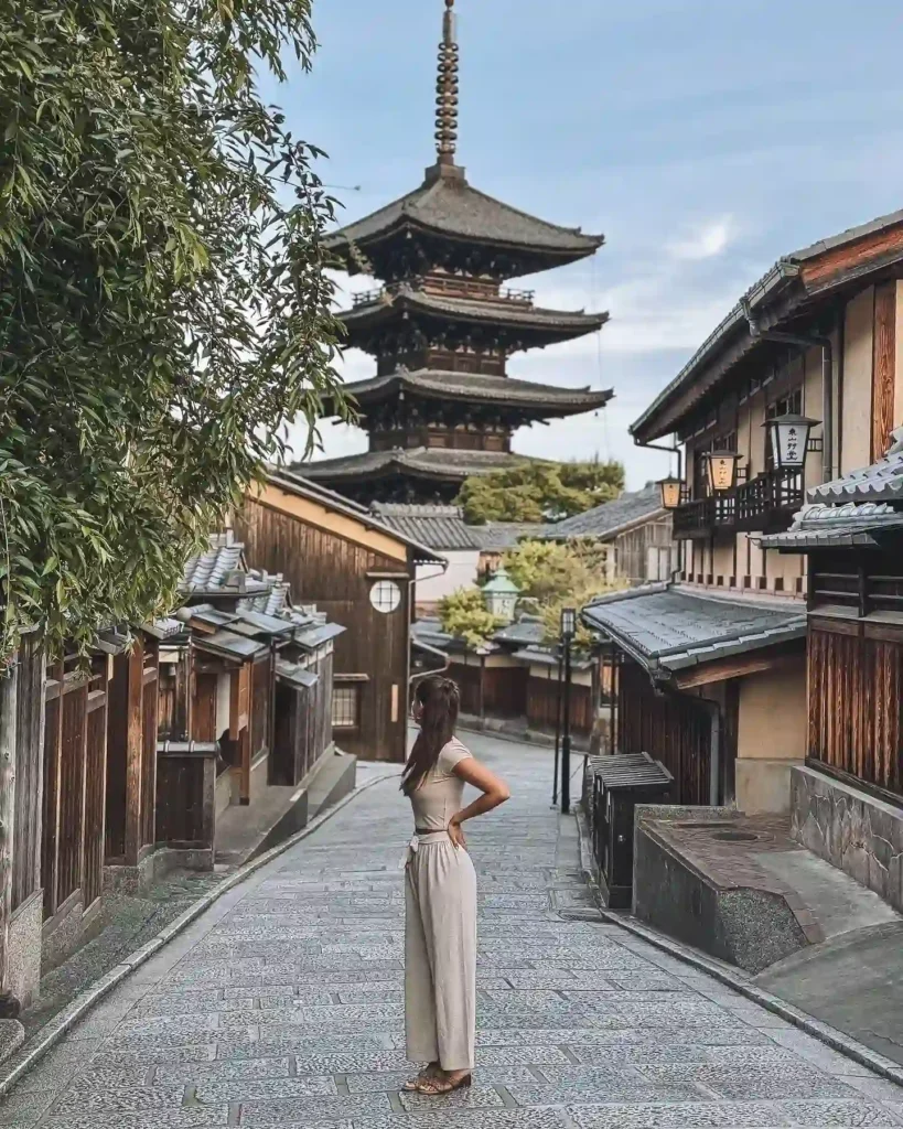 A woman stands in a historic Kyoto street, admiring a traditional pagoda and charming wooden buildings.