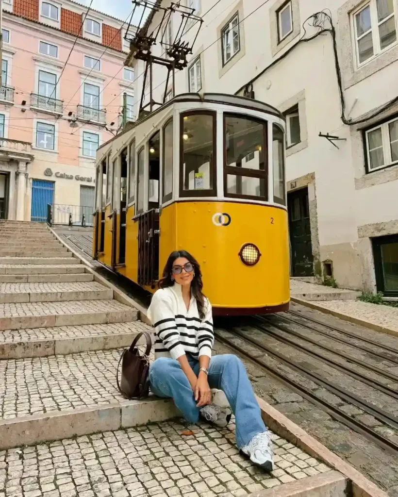A woman sits on steps beside a yellow tram in a picturesque Lisbon street, showcasing urban charm and style.